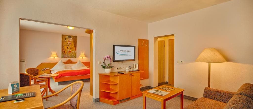 Suite living room with sofa and dining area, flat-screen TV, opening onto the bedroom